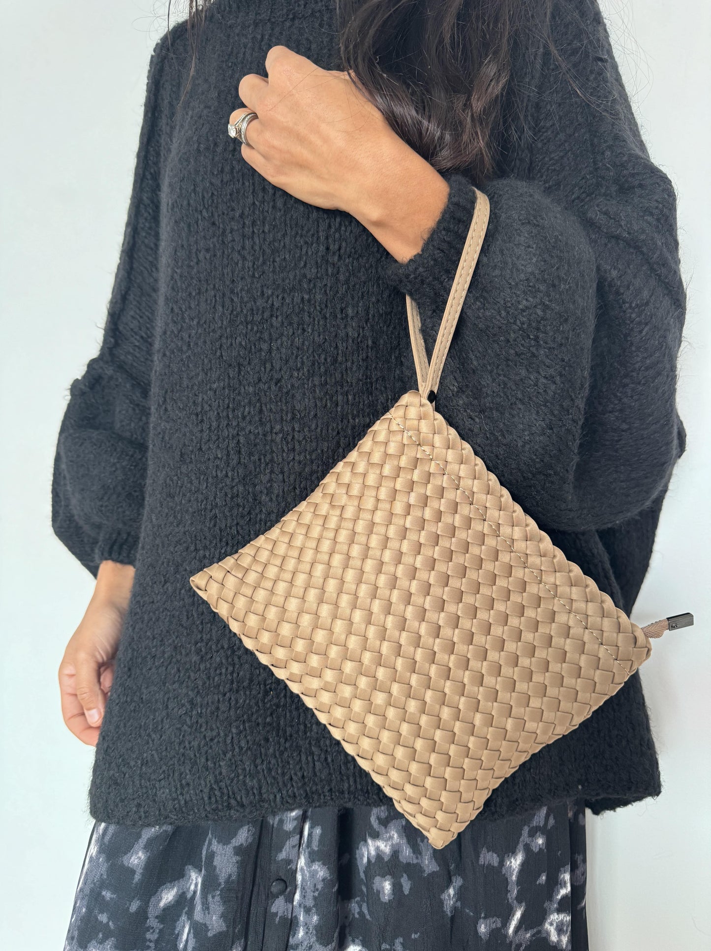 Pochette Sacs Tega en teinte camel avec un design tressé, portée avec un pull pour une touche de sophistication discrète.