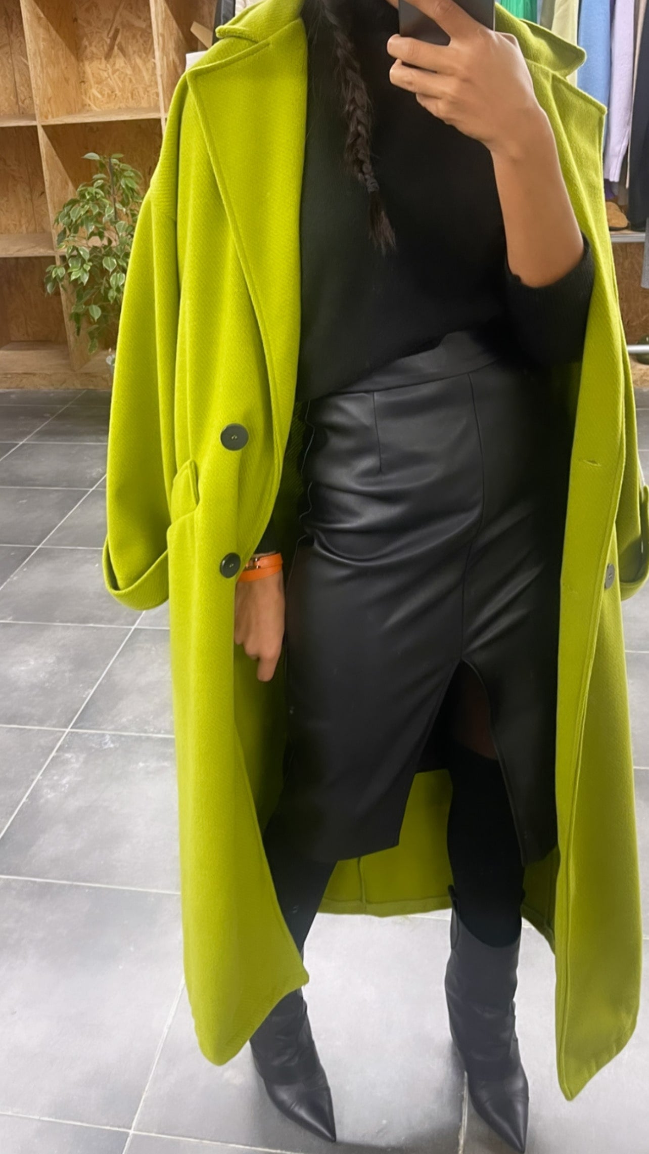 jupe crayon en similicuir noir portée avec un manteau vert fluo et bottes noires