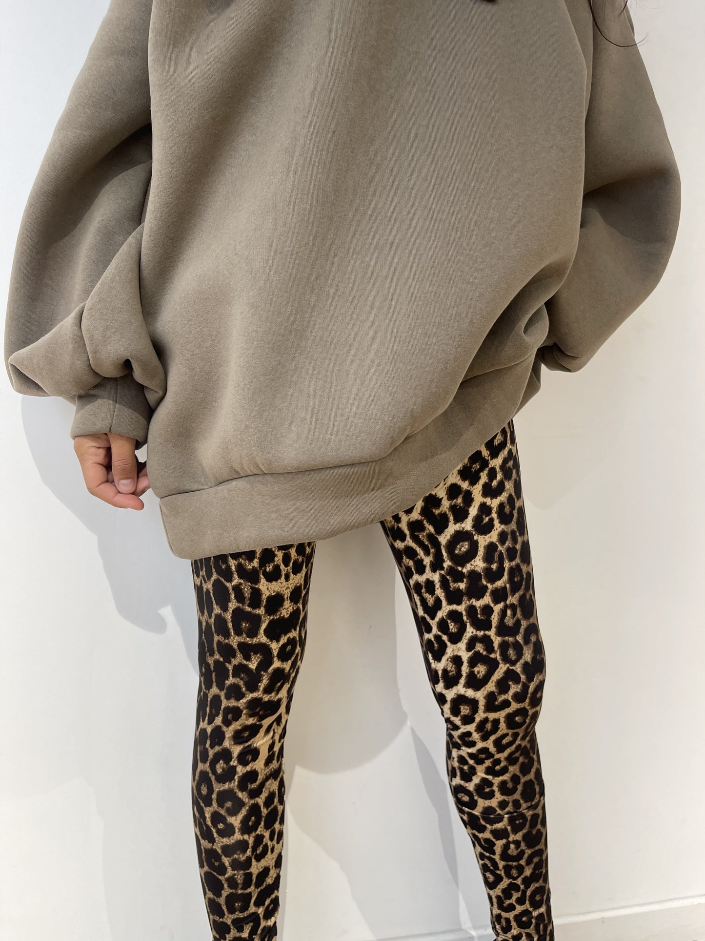 Legging léopard pour femme, associé à un sweat oversize kaki et des baskets noires.