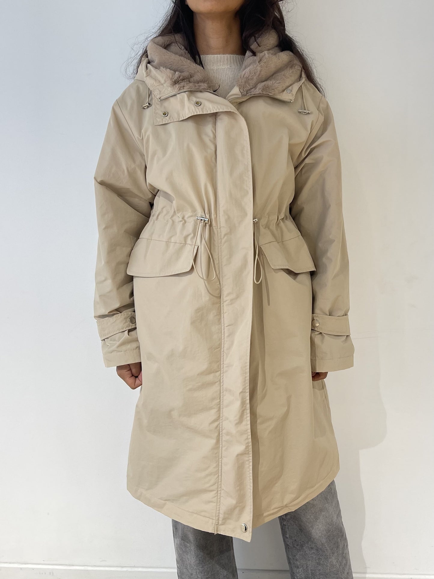 Manteau imperméable beige pour femme, avec capuche fourrée, cordon ajustable et poches à rabat.