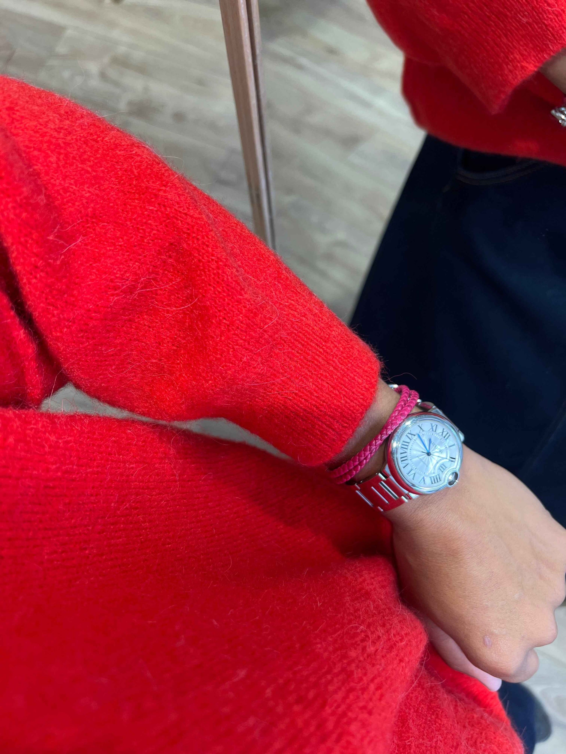 Détail du pull en laine rouge avec montre et bracelet rose.