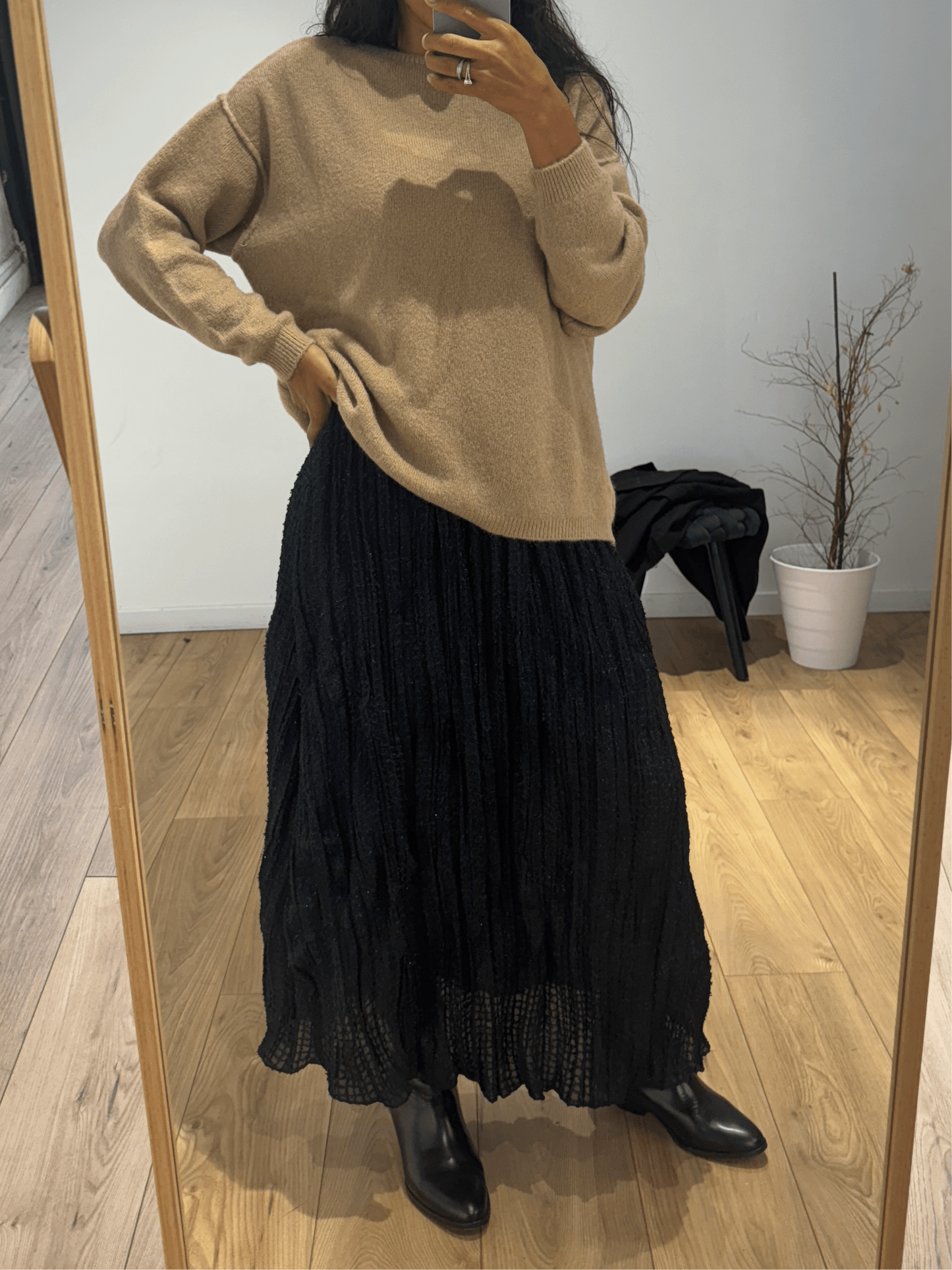 Femme portant un pull en laine beige avec une jupe longue noire plissée.