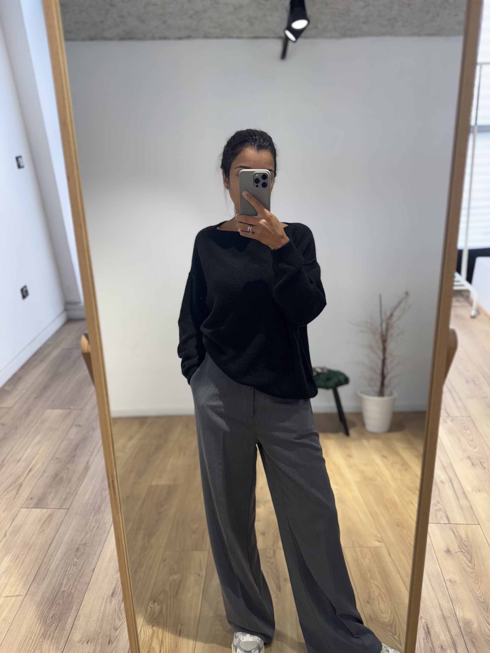 Femme en pull en laine noir avec un pantalon gris large et des baskets blanches.