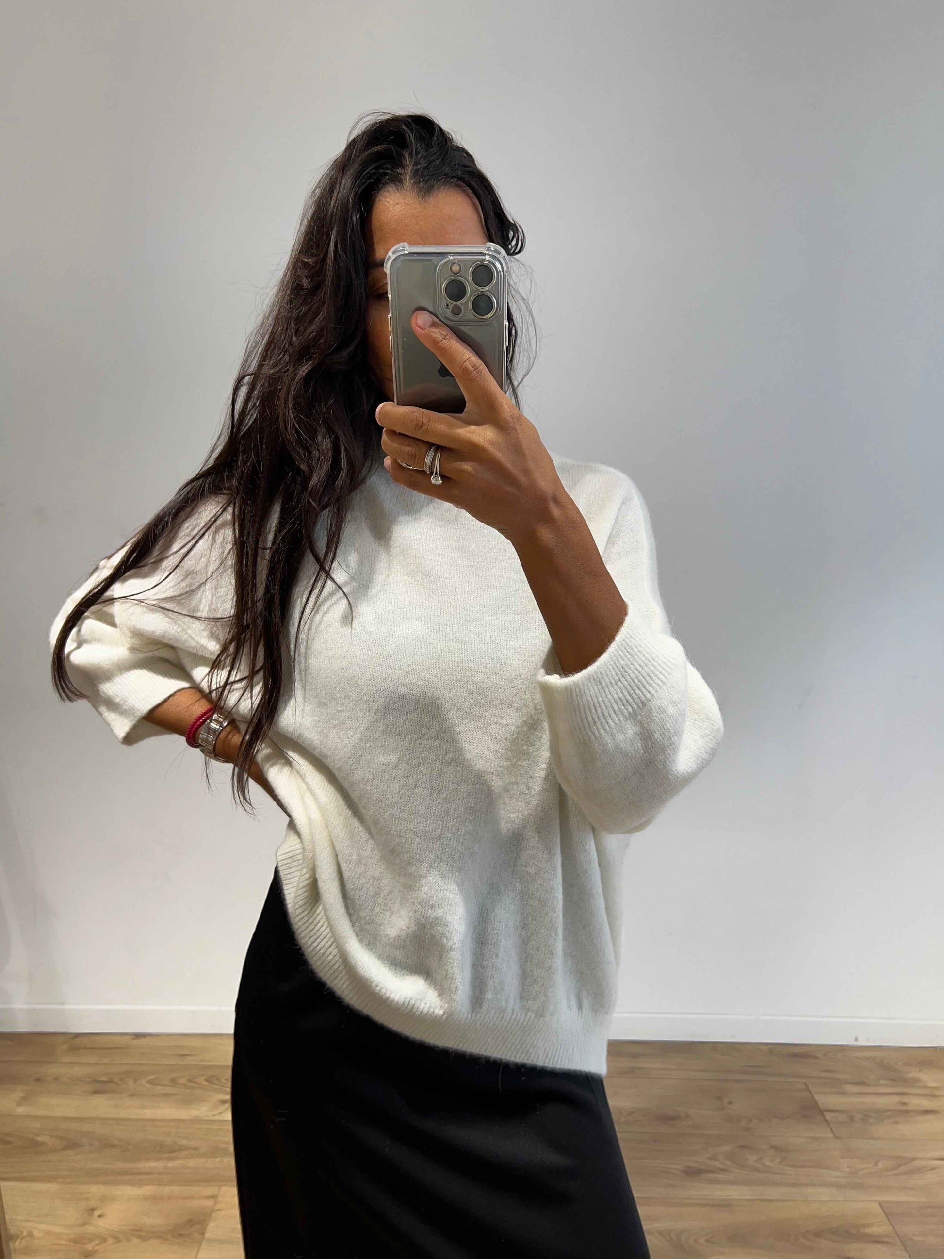 Femme portant un pull blanc à manches trois quarts avec jupe longue, style élégant.