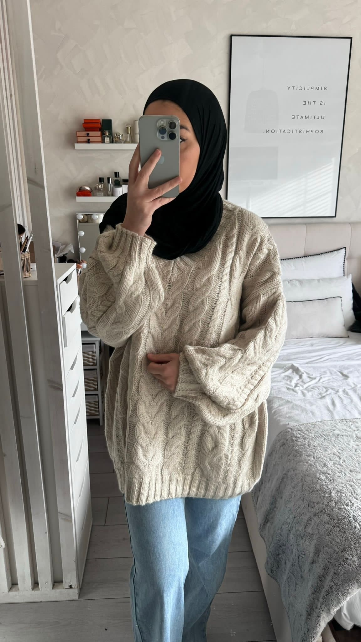 Femme portant un pull oversize en maille torsadée crème devant un miroir