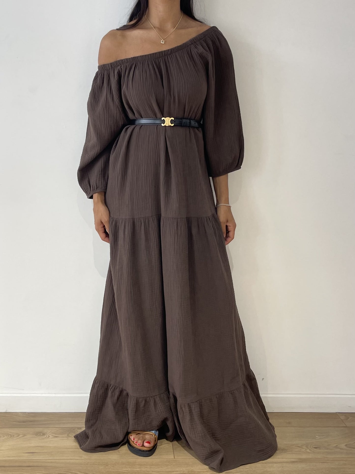 Femme portant une robe marron en gaze de coton avec épaules dénudées et ceinture noire.