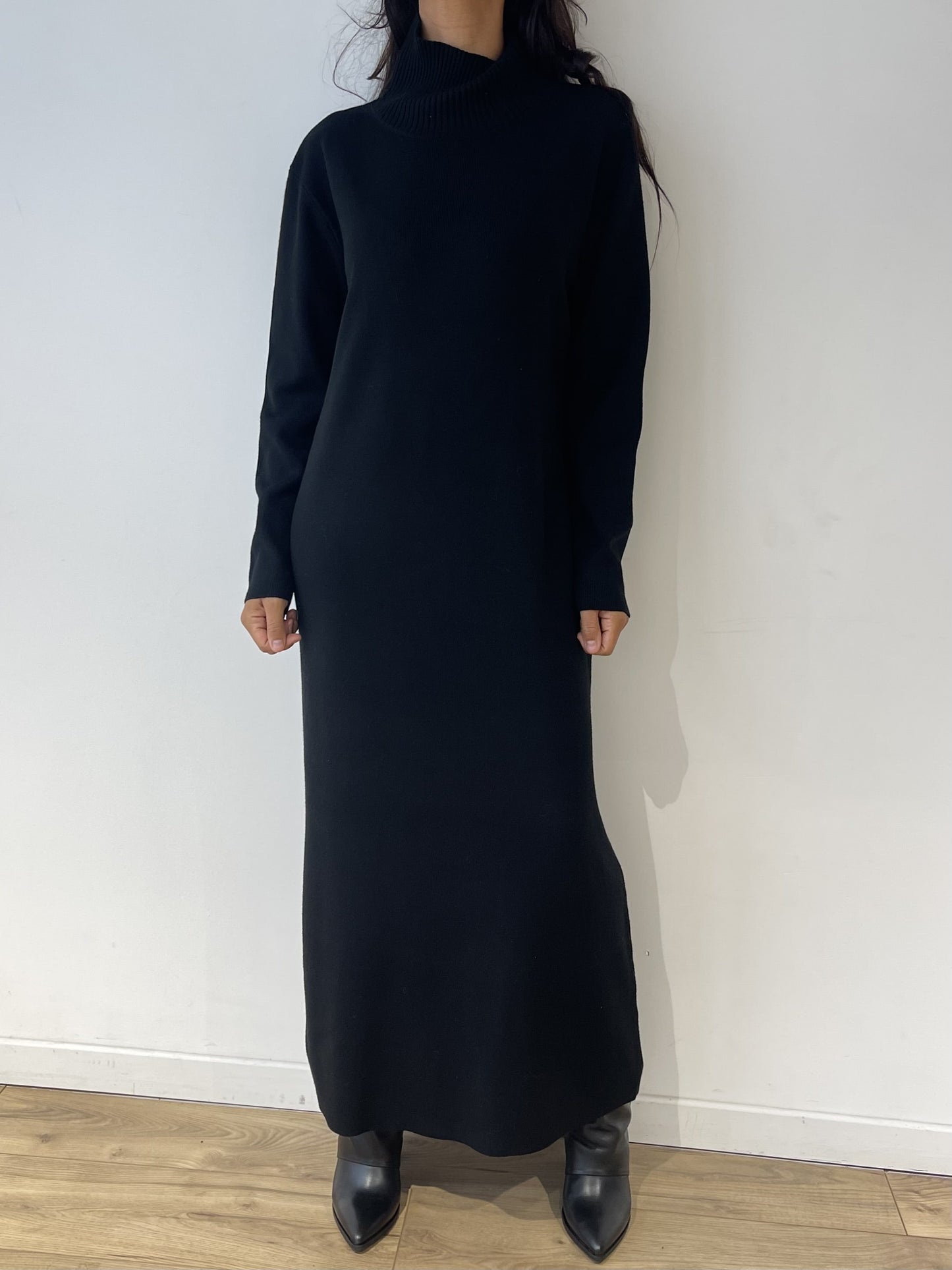 Robe noire longue en maille, manches longues, portée avec bottines noires.