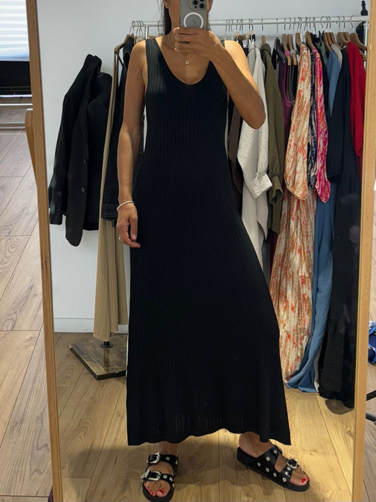 Femme portant une robe longue noire sans manche devant un miroir.